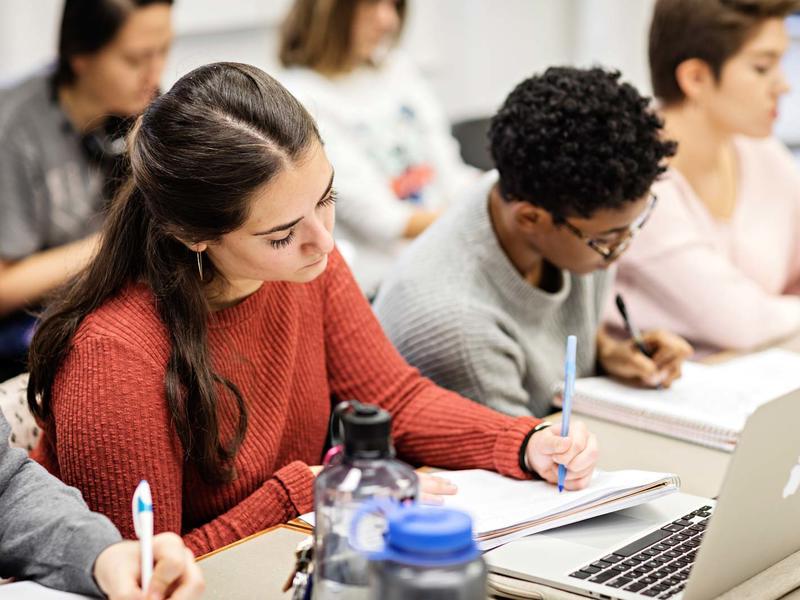 students in class taking notes by hand in notebooks